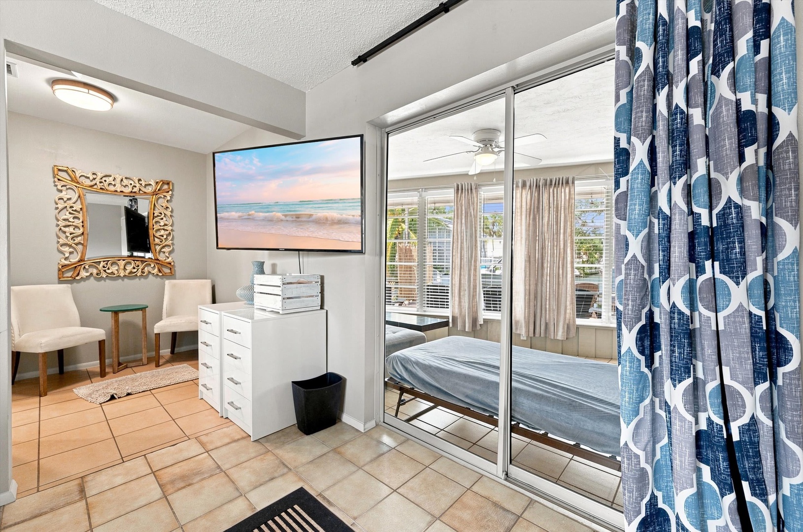 Step into your sunlit retreat where warm tile floors meet beach-inspired décor. Through sliding glass doors, your private bedroom awaits with inviting coastal charm and bright natural light.