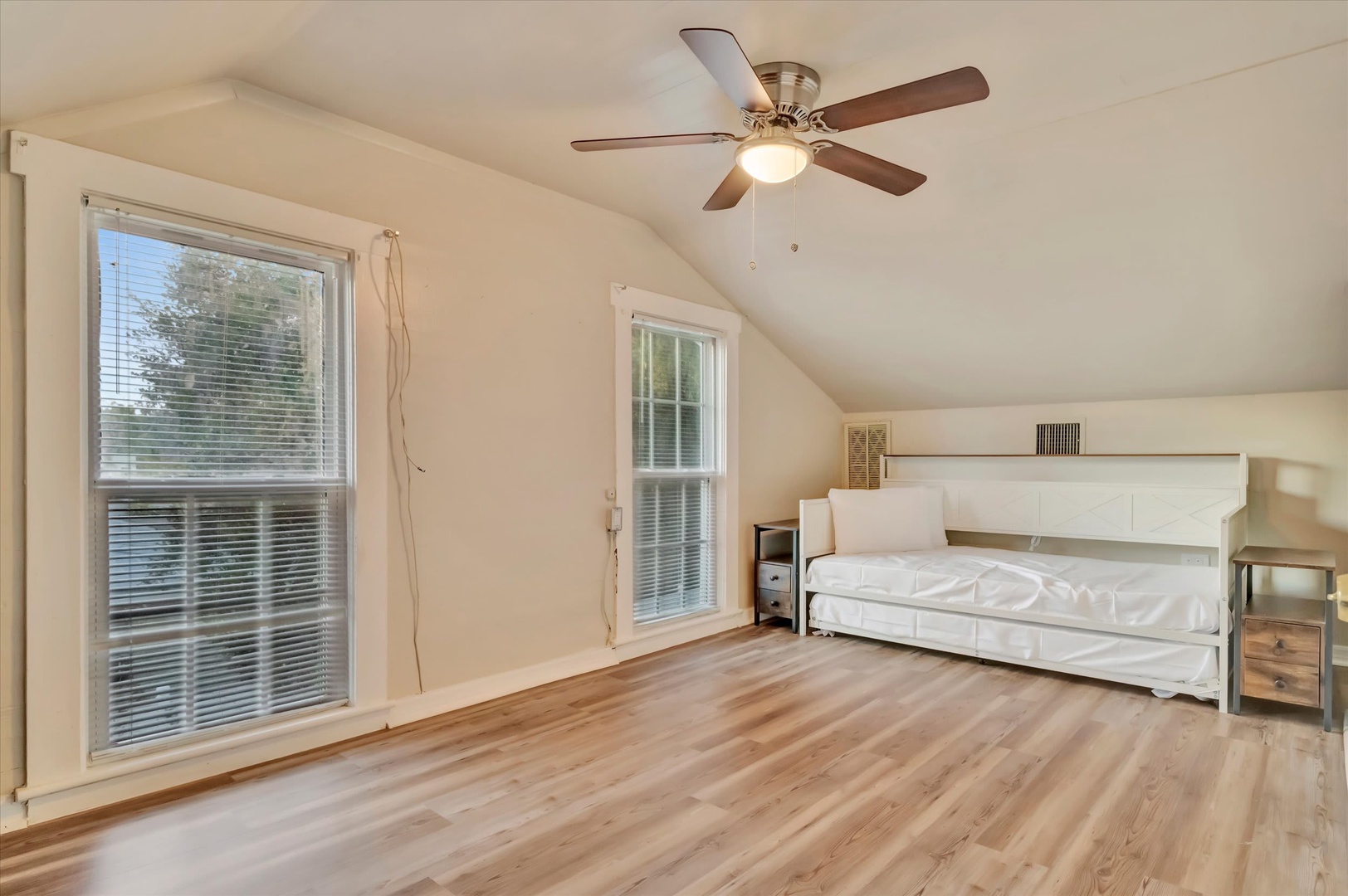 Your bright bedroom retreat features warm wood floors, fresh white walls, and vaulted ceilings with a ceiling fan. Natural light pours through generous windows, creating a peaceful sanctuary for restful nights.