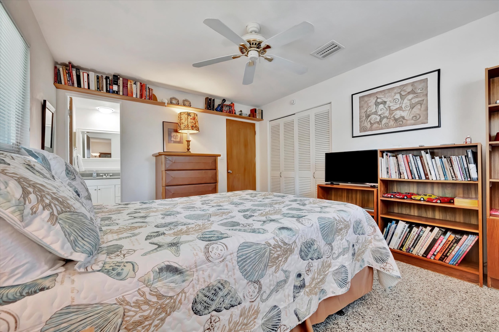 Your bright, book-filled bedroom welcomes you with soft coastal tones, a plush queen bed, and a ceiling fan to keep you comfortable all night long.