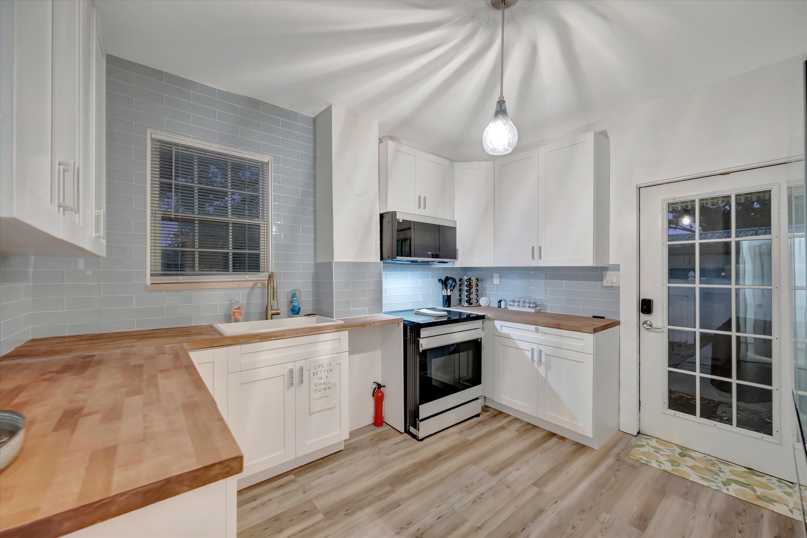 Step into your bright, airy kitchen with butcher-block counters and pale blue tile. Light wood floors warm the space, while a charming pendant overhead creates a cozy spot for preparing homemade meals.