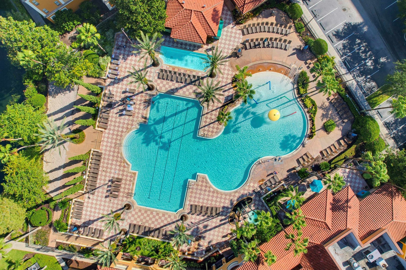 Aerial view of the resort-style pool complex, featuring a freeform lagoon pool, separate spa area, and sunbathing deck surrounded by palm trees and lounge chairs.