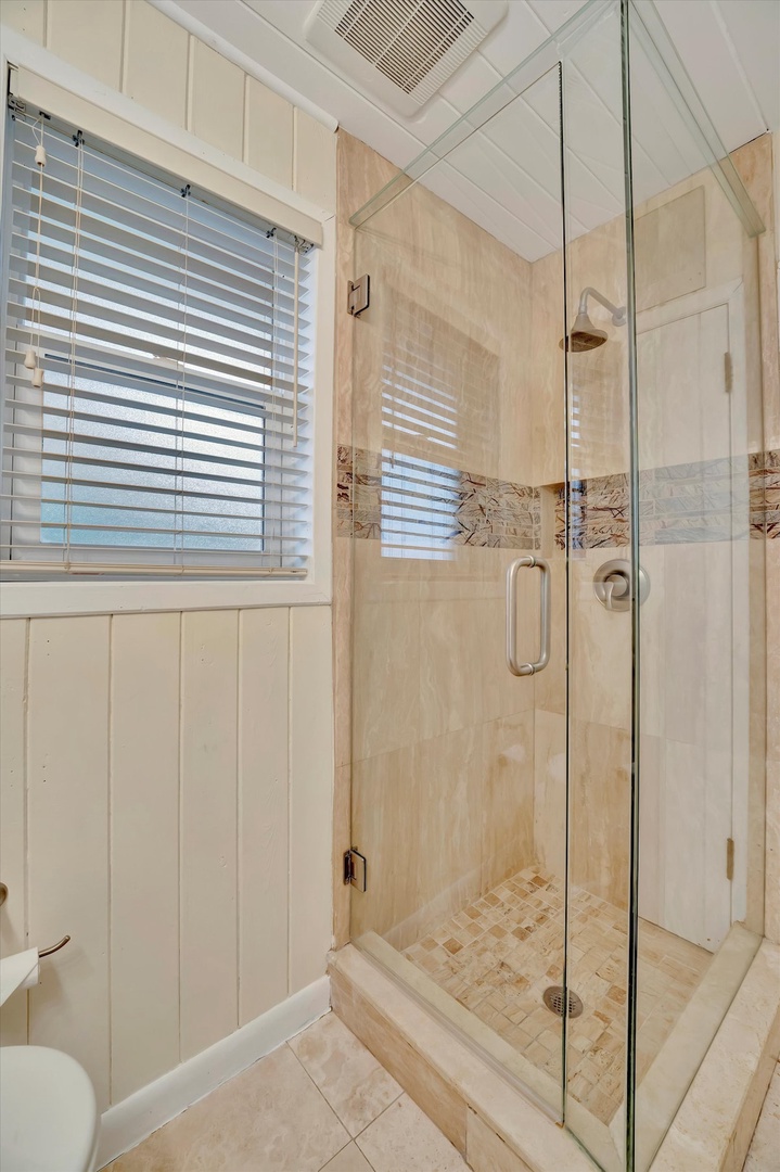 Step into your beautifully tiled walk-in shower with frameless glass doors, combining coastal charm with modern comfort. Natural light brightens this inviting space for a refreshing start to your day.