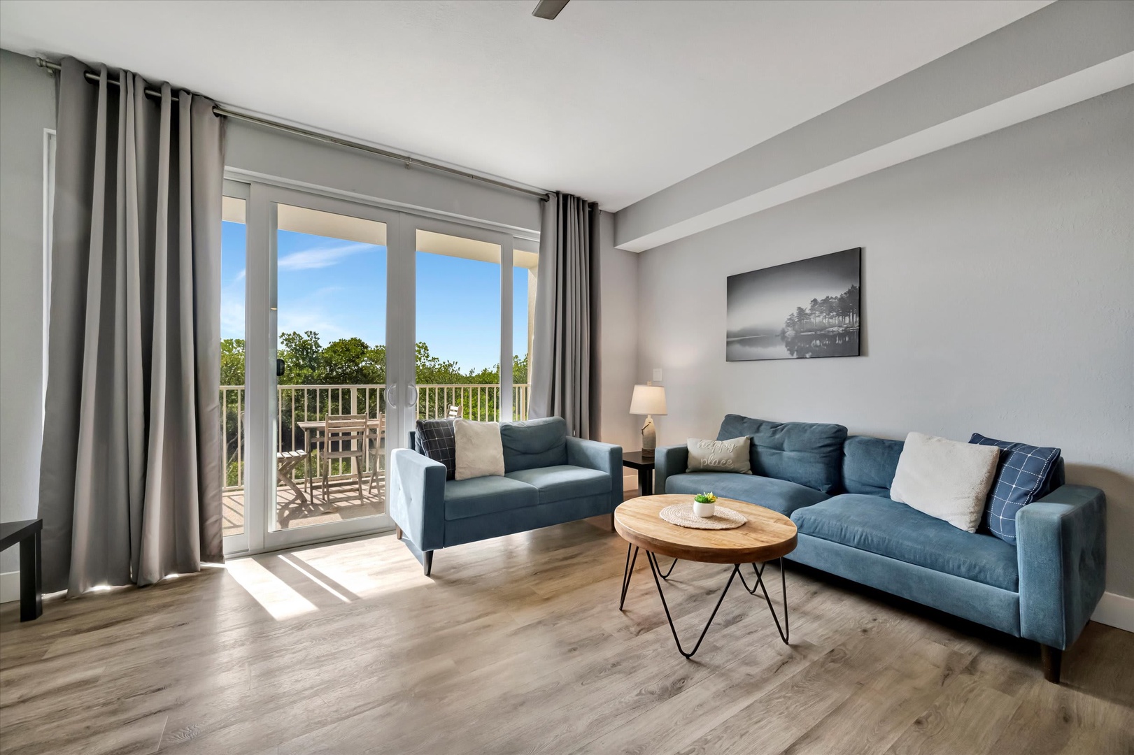 Settle into your bright, modern living room where natural light spills through glass doors opening to your private balcony. Sink into plush seating and enjoy peaceful tree-lined views perfect for morning coffee or evening relaxation.