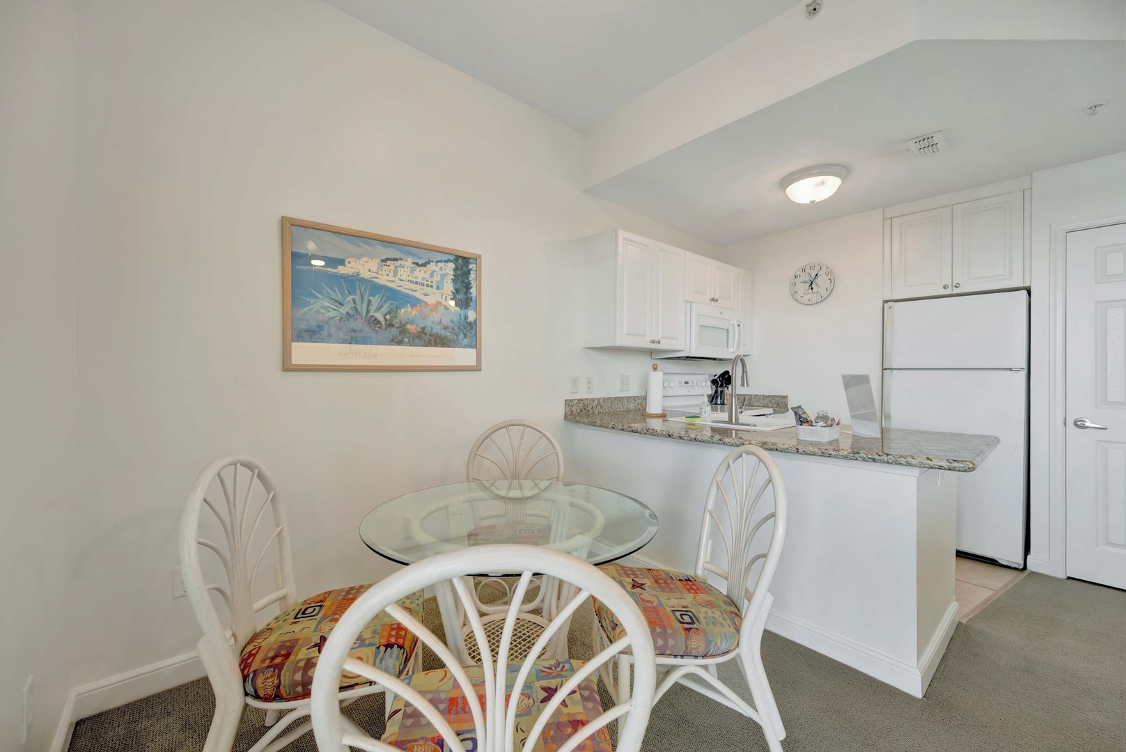 Bright, open kitchen and dining area with a glass-top table, granite counters, and full-sized appliances—perfect for gathering after a beach day or preparing a simple meal.