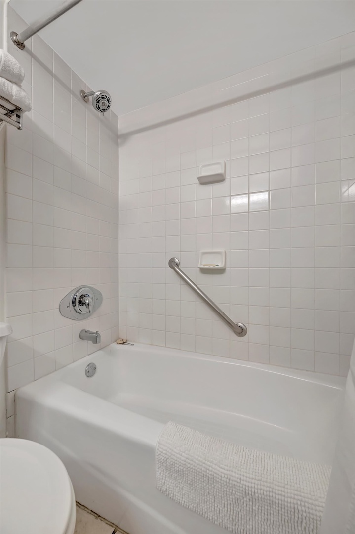 A clean, accessible tub-shower combo awaits in your bright bathroom, complete with a safety grab bar and thoughtful touches for a comfortable stay.