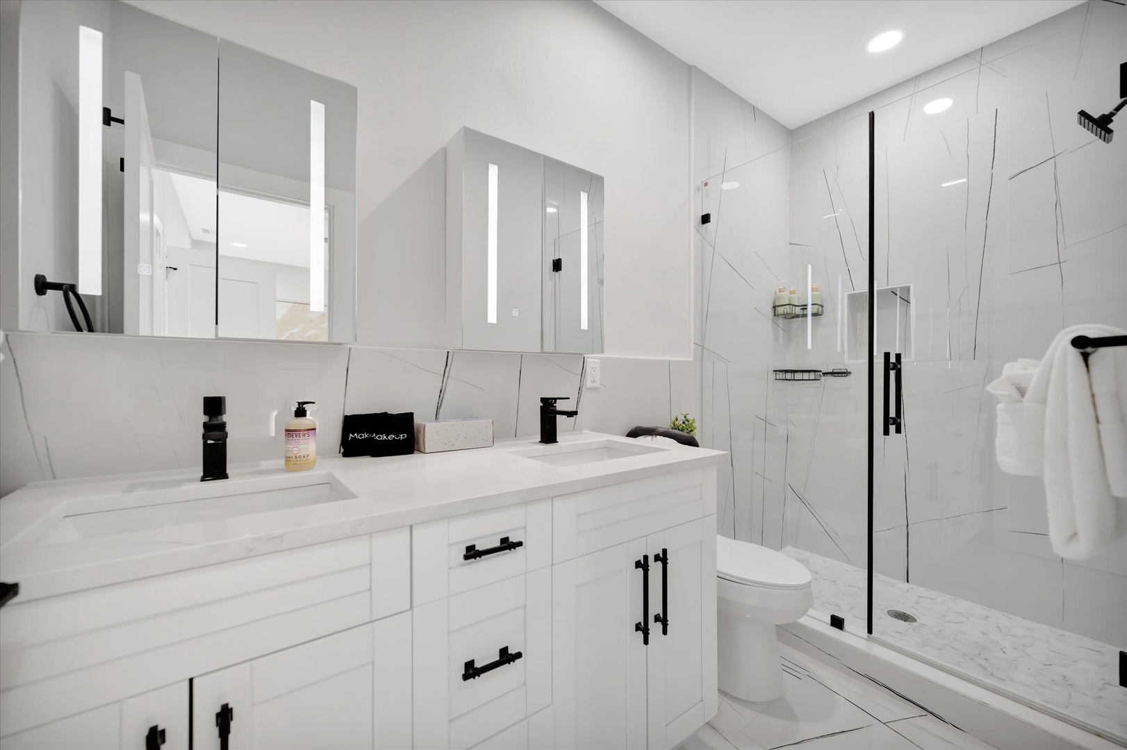Step into your modern spa-like bathroom with sleek marble-look tile, a spacious glass-enclosed shower, and a bright double-sink vanity with stylish black fixtures.