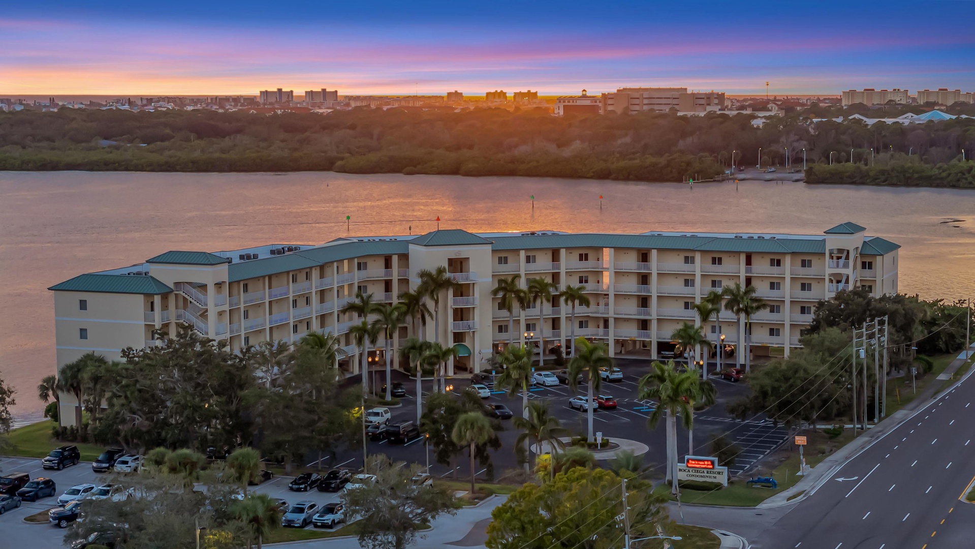 Aerial view of the property overlooking a waterfront location at dusk, with palm trees and parking areas visible.