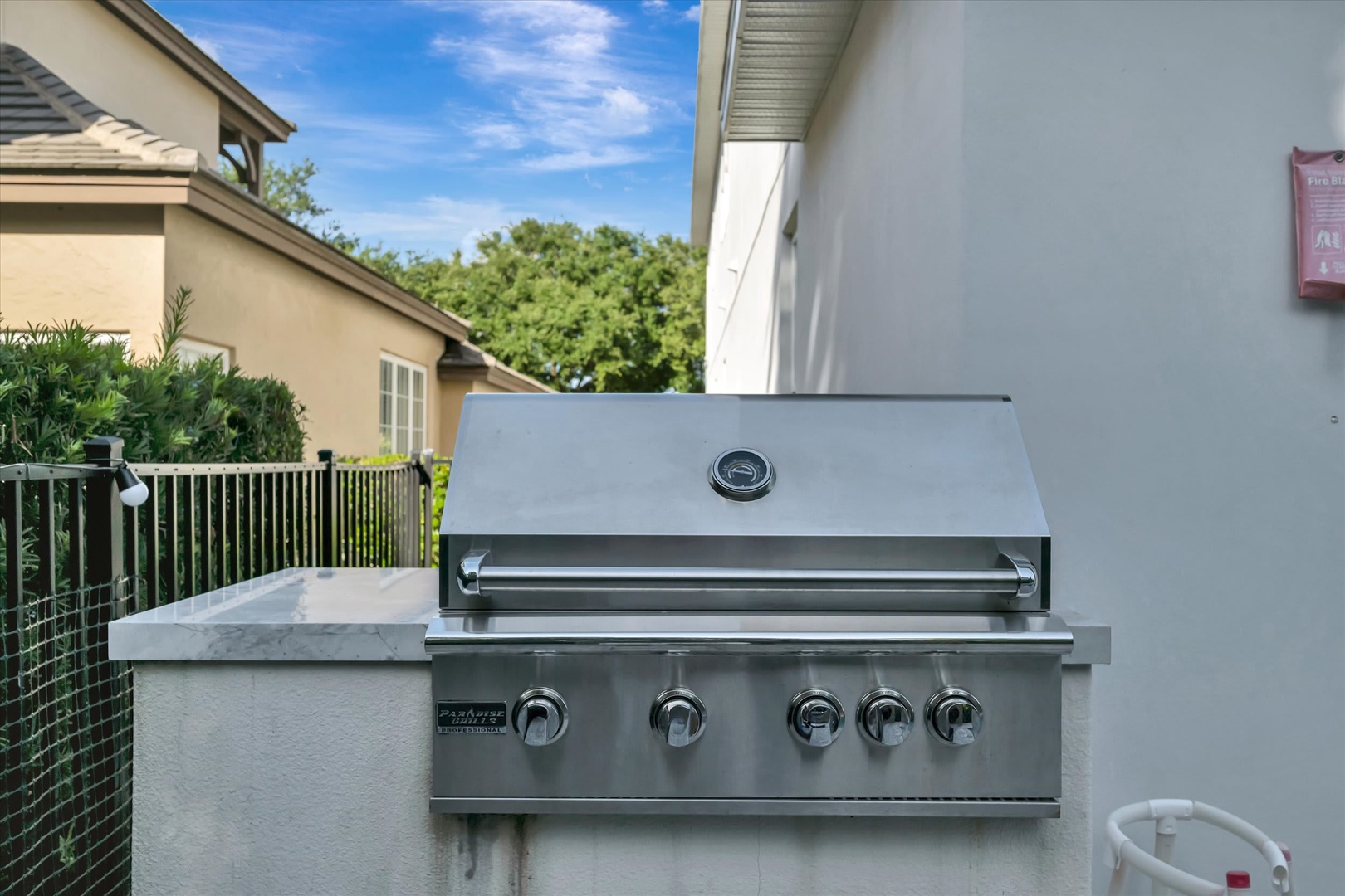 Fire up the grill and savor your meals al fresco with this built-in outdoor kitchen, perfectly positioned under blue skies and surrounded by lush greenery.
