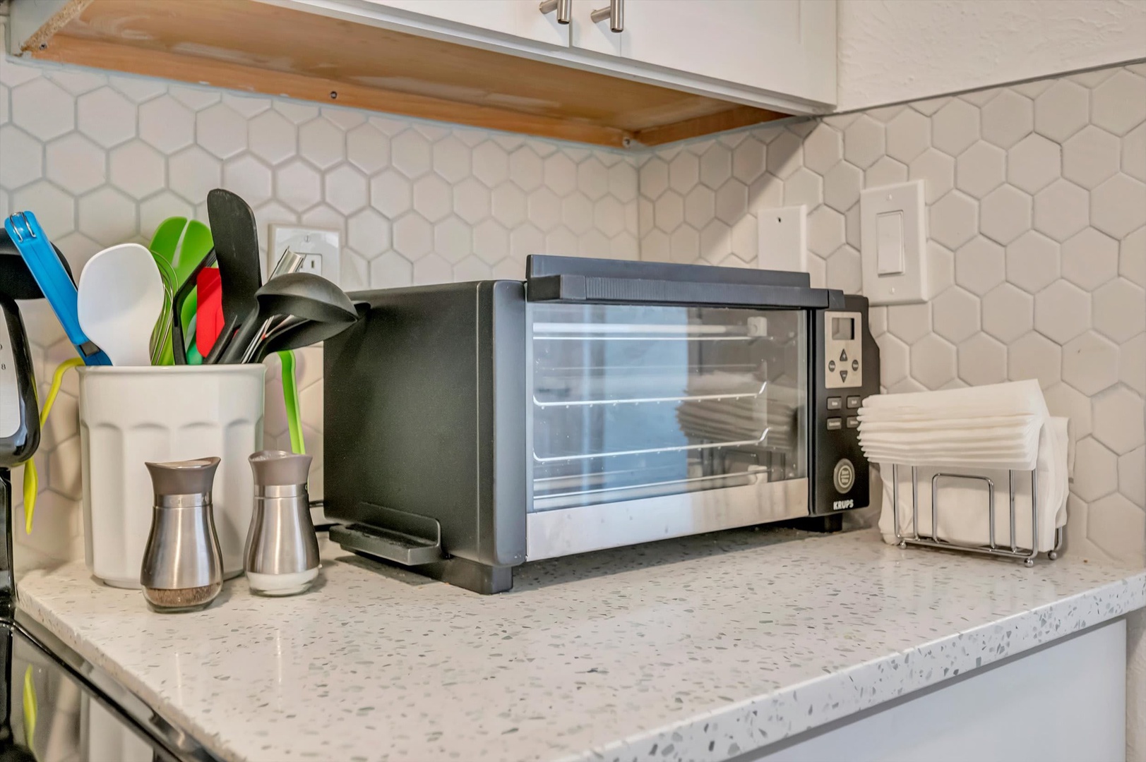 Your bright kitchen counter features a toaster oven, utensils, and charming hexagonal tile backsplash—everything you need to prepare quick meals and feel right at home.