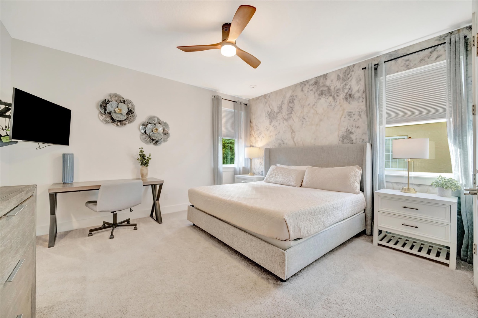Rest easy in your serene bedroom, where soft neutral tones and plush linens create a peaceful retreat. Natural light filters through the windows, warming the space as you unwind beneath the gentle breeze of the ceiling fan.