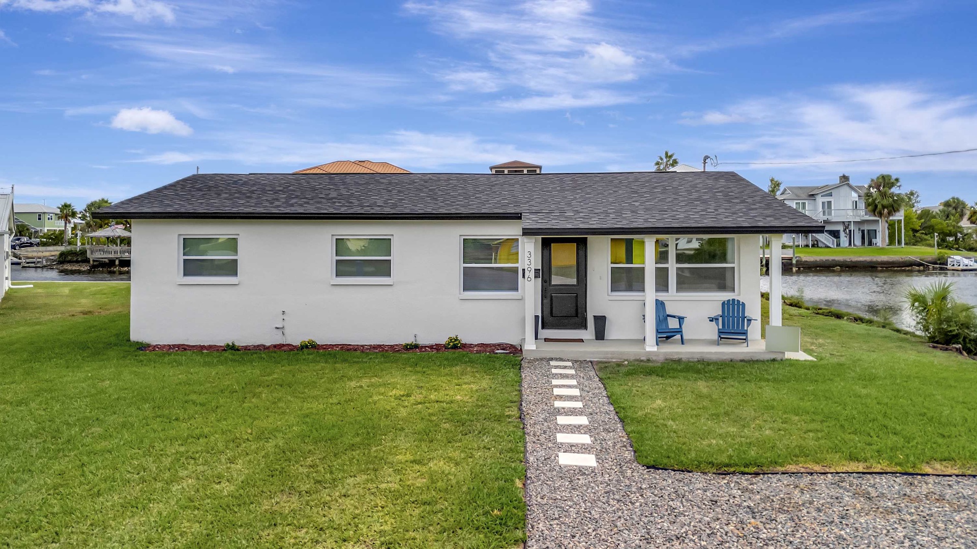 A welcoming waterfront retreat with charming blue Adirondack chairs beckoning you to unwind beside the canal. Step through the garden pathway to your peaceful escape with views of palm-dotted shores.