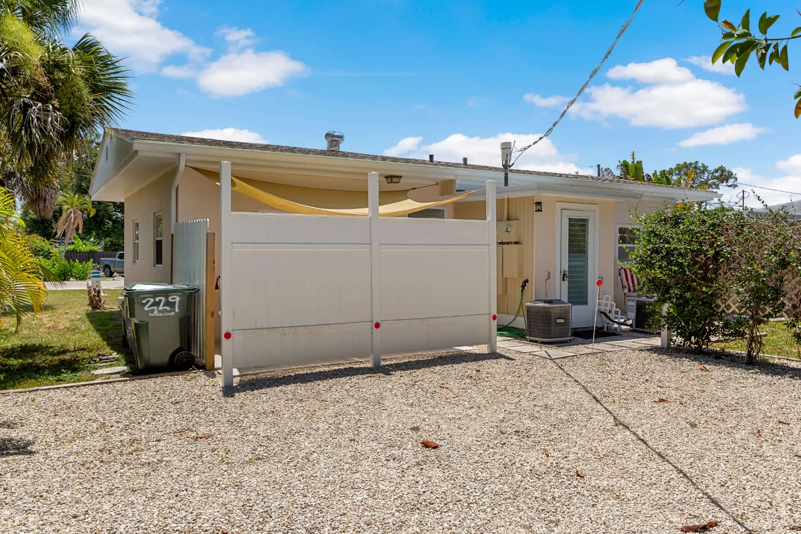 This charming beach cottage offers easy parking and a quiet outdoor entry area, surrounded by lush tropical greenery and bright Florida sunshine.