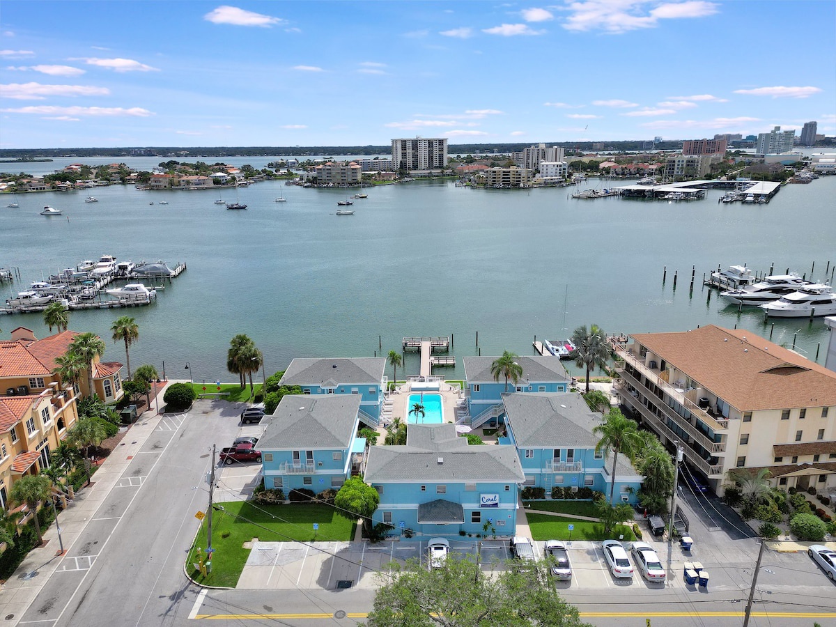 Waterfront property featuring direct marina access, swimming pool, and palm-lined grounds along a protected bay with boat docks and coastal skyline views.