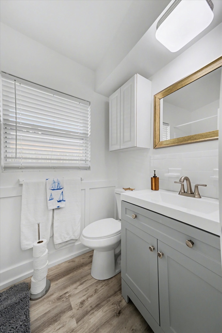 Your bright, coastal-style bathroom combines functionality with charm, featuring warm wood-tone flooring and crisp white finishes that create a fresh, inviting space for your morning routine.