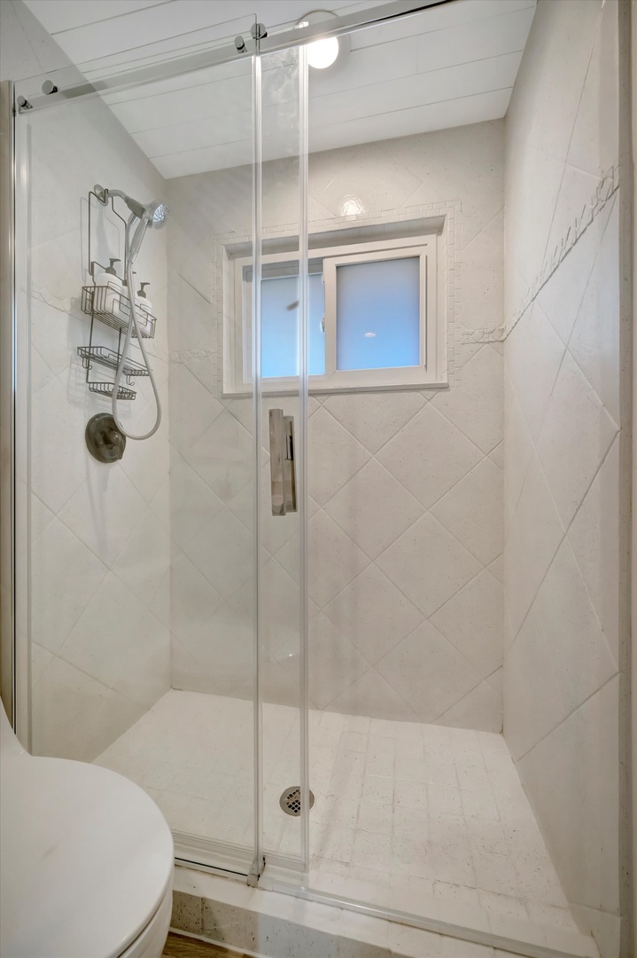 Step into your sleek, modern shower with crisp white tile and a refreshing rainfall showerhead. The frameless glass door and clean lines create a spa-like retreat, while the window above fills the space with natural light.