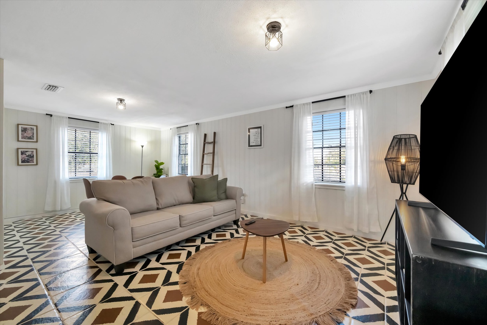 Sink into the plush sofa and feel instantly at home in this bright, stylish living room where bold geometric tiles and soft natural light create a warm, inviting retreat for your stay.
