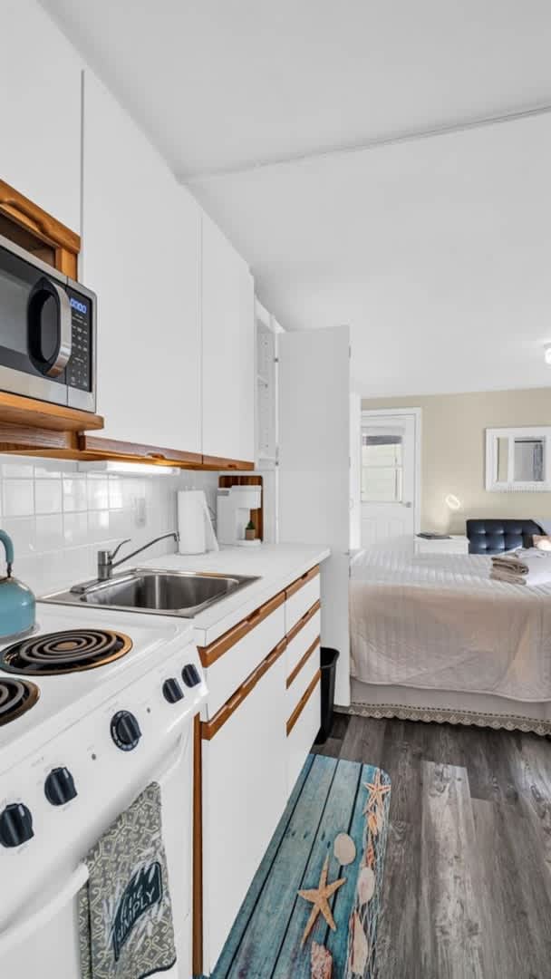 Your cozy studio features a compact kitchen with everything you need—microwave, stove, and sink—plus a comfortable sleeping area just steps away. Warm wood accents and beachy touches create a welcoming retreat.