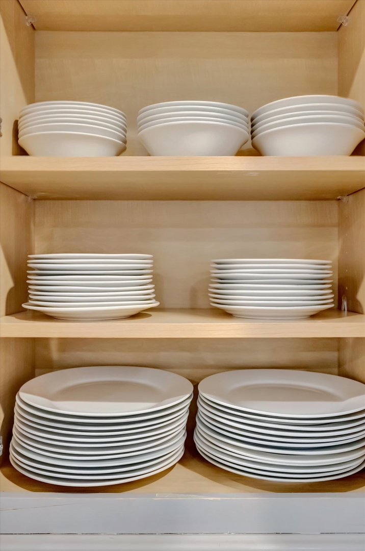 Your kitchen comes fully stocked with generous place settings — crisp white dishes and bowls all neatly arranged and ready for family dinners or easy entertaining.