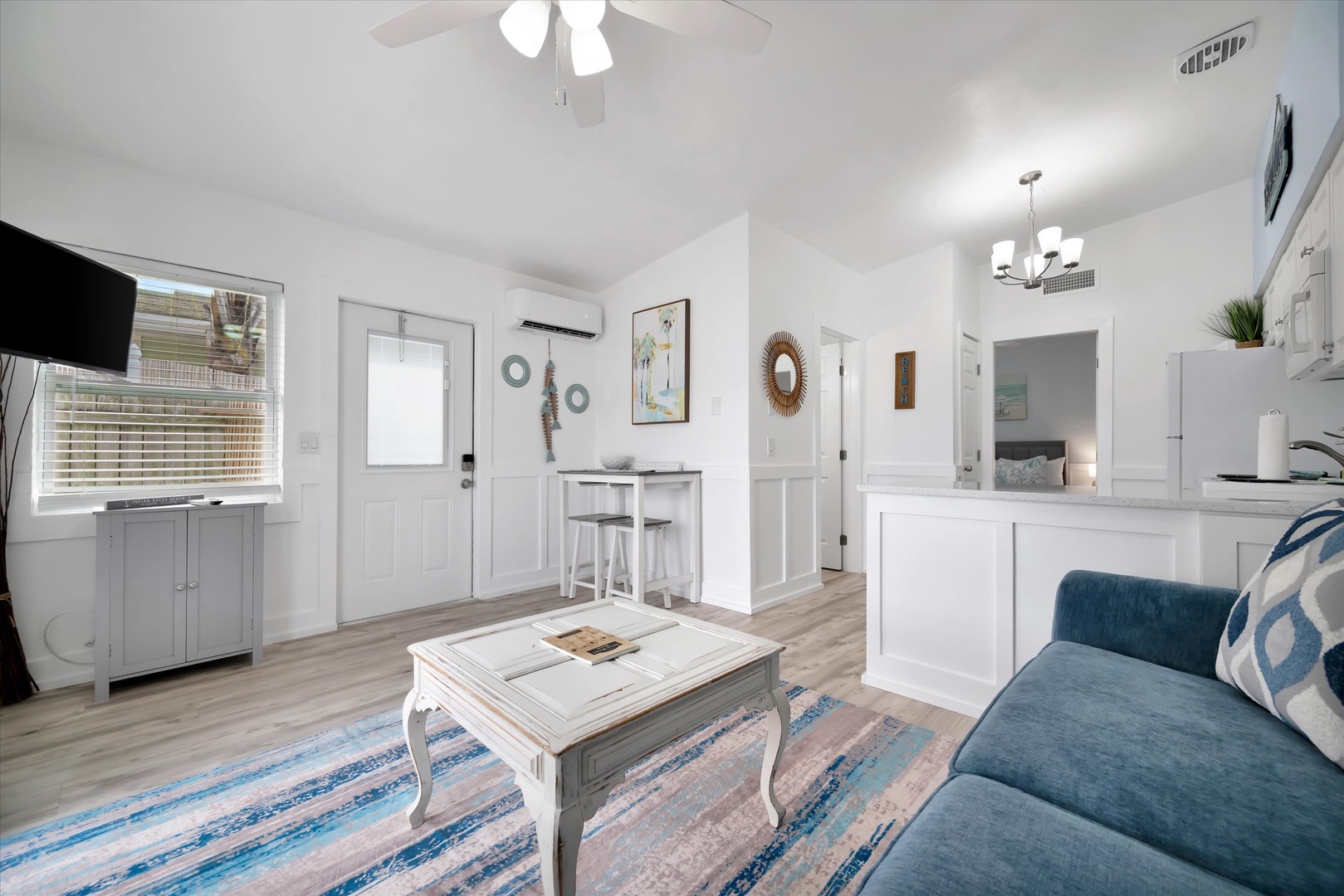 Step into this bright, coastal-inspired living space where light wood floors and crisp white walls create your perfect beach retreat. Relax on the plush sofa, enjoy your favorite shows, or gather around the table for meals and games.
