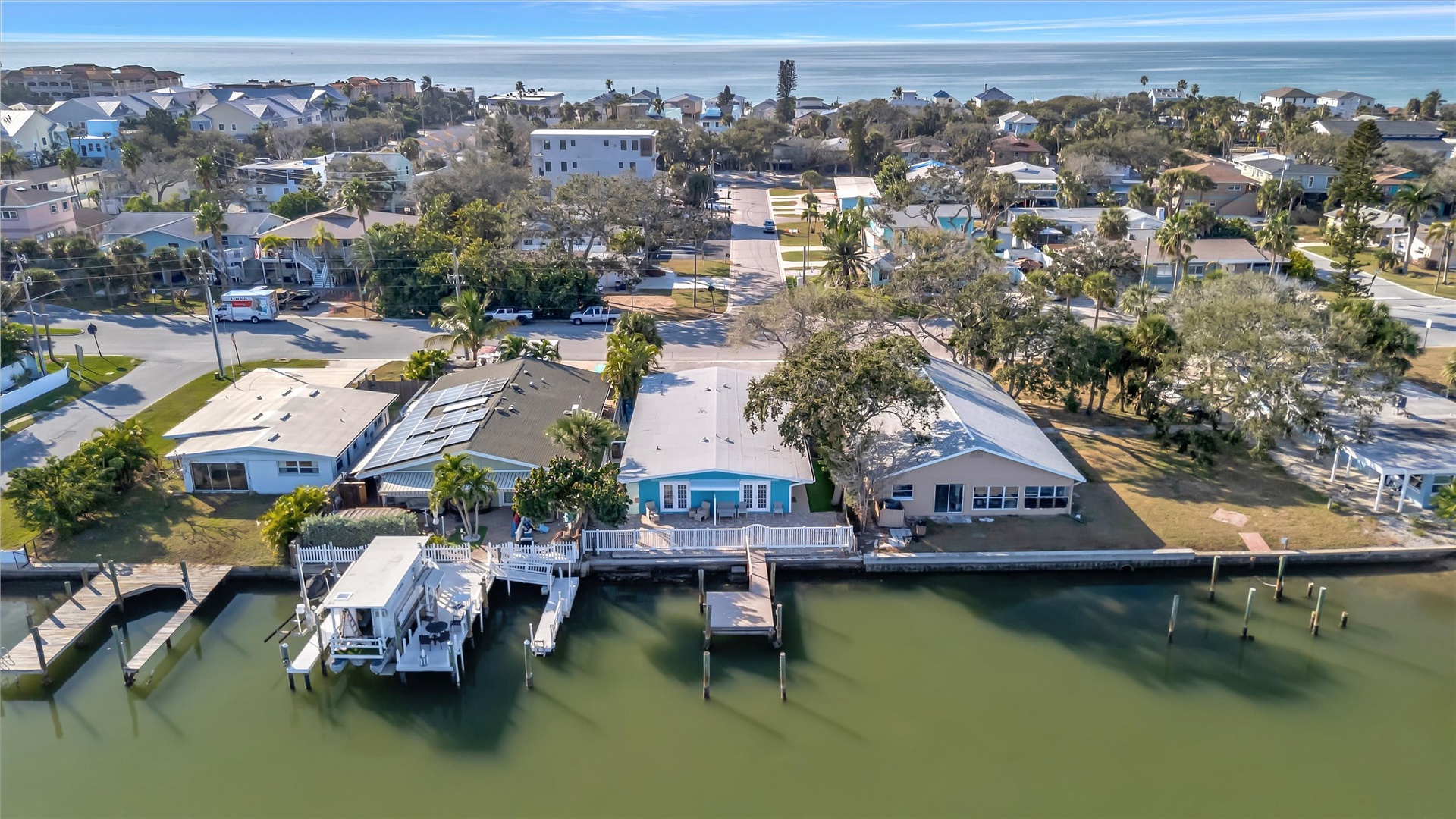 Aerial view of waterfront properties with private docks and boat slips in a coastal residential neighborhood. The ocean stretches across the horizon beyond the community.