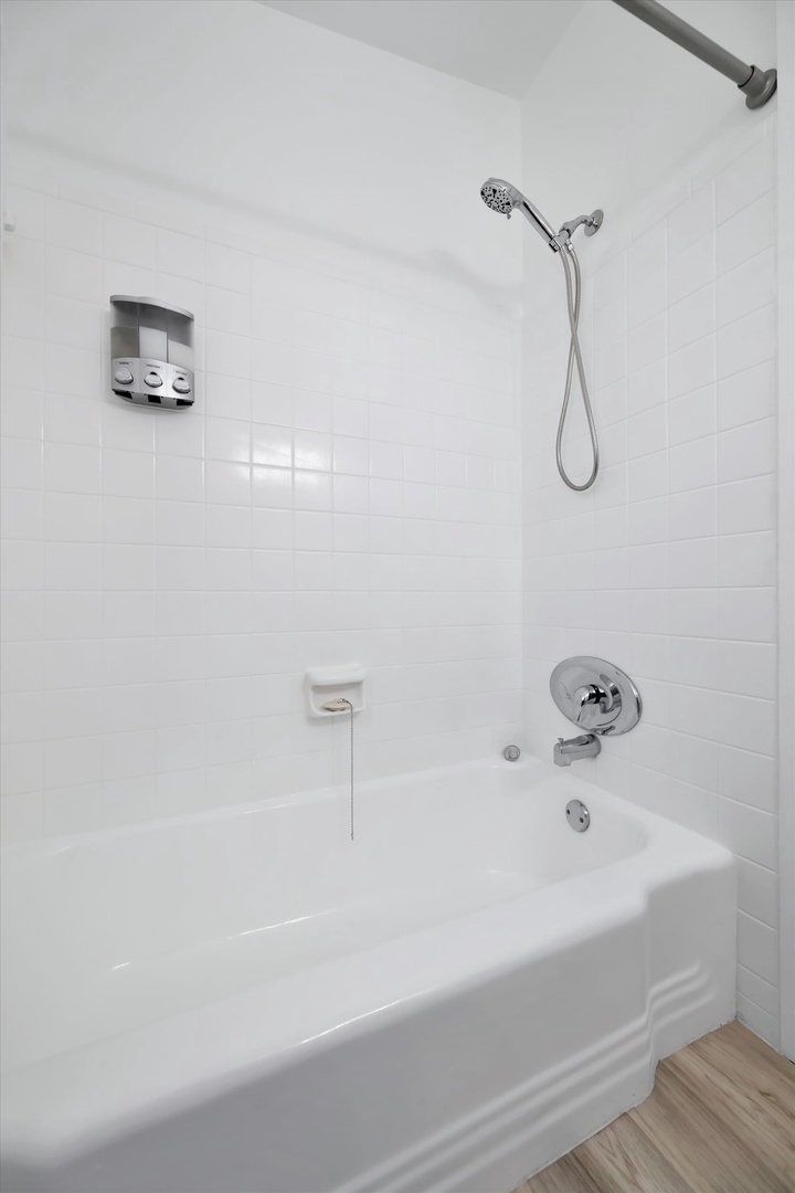 Spotless white tiled bathroom with a tub-shower combo, gleaming fixtures, and convenient wall-mounted amenities to make your stay comfortable and refreshing.