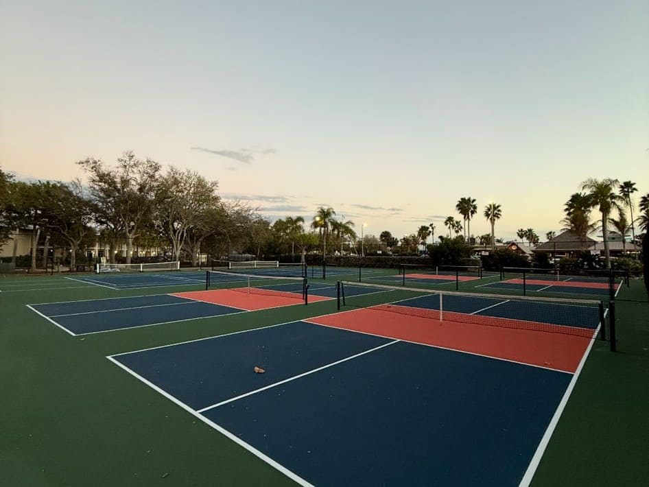 Multiple tennis courts available on-site with pristine playing surfaces, set against a backdrop of palm trees and a tranquil evening sky.