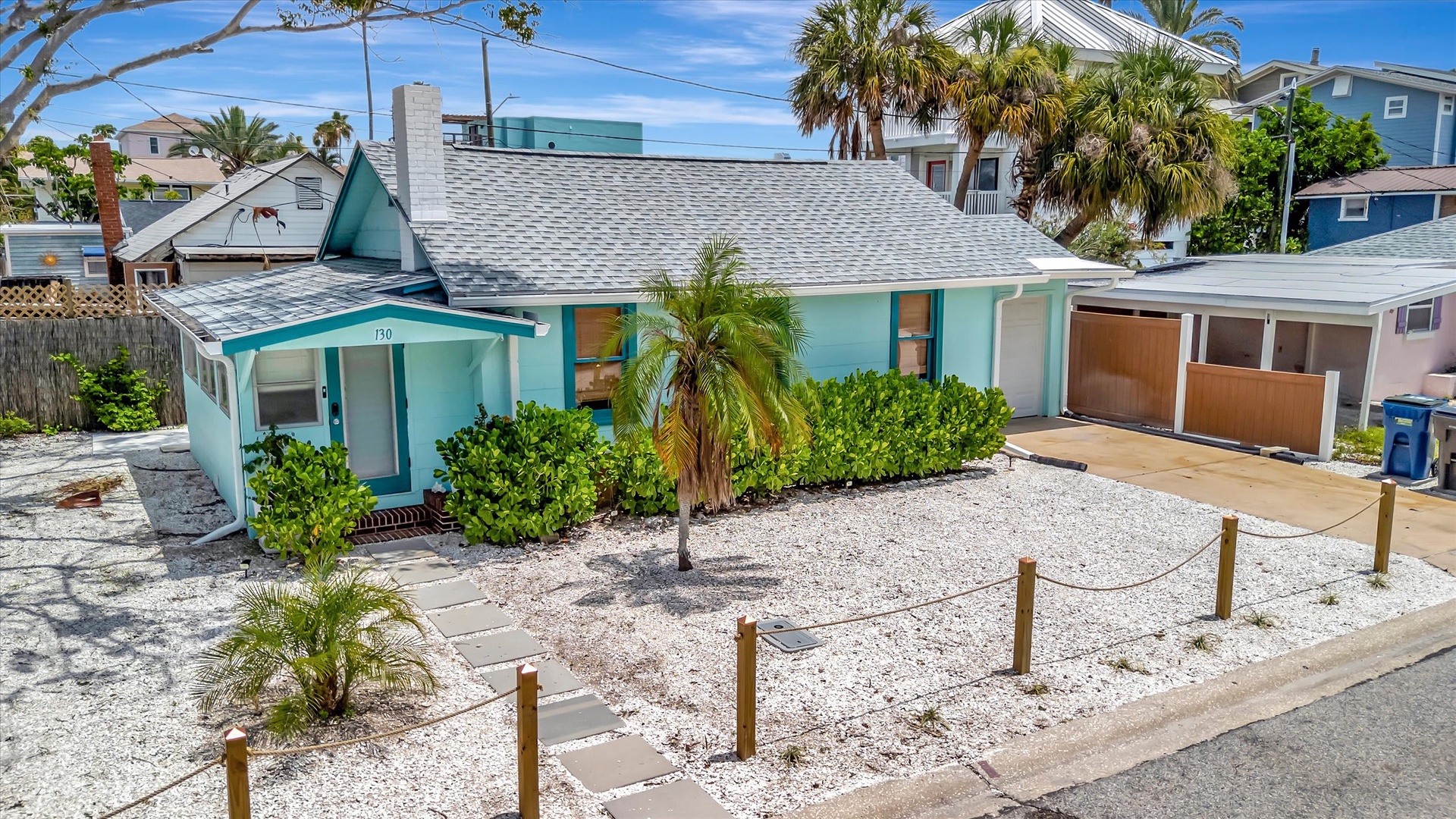 Cheerful turquoise beach cottage surrounded by swaying palms and tropical landscaping in a vibrant coastal neighborhood.