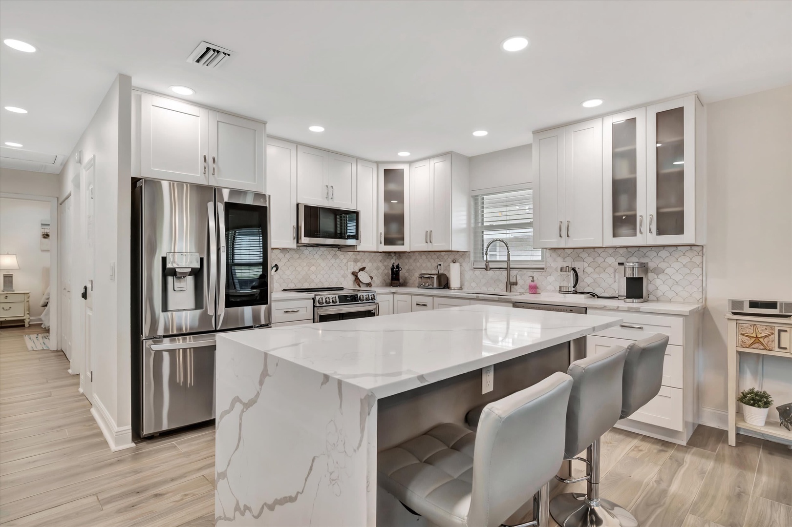 Picture yourself whipping up meals in this bright, modern kitchen with gleaming white quartz countertops, stainless steel appliances, and a spacious island perfect for morning coffee or casual dining.