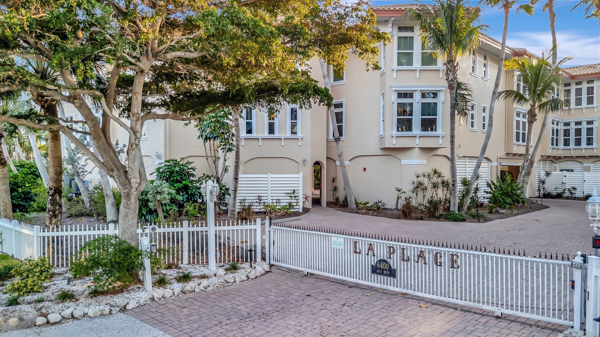 Laplace beach townhomes nestled among tropical palms and mature shade trees, located in a private gated community along the waterfront. A serene coastal neighborhood setting.