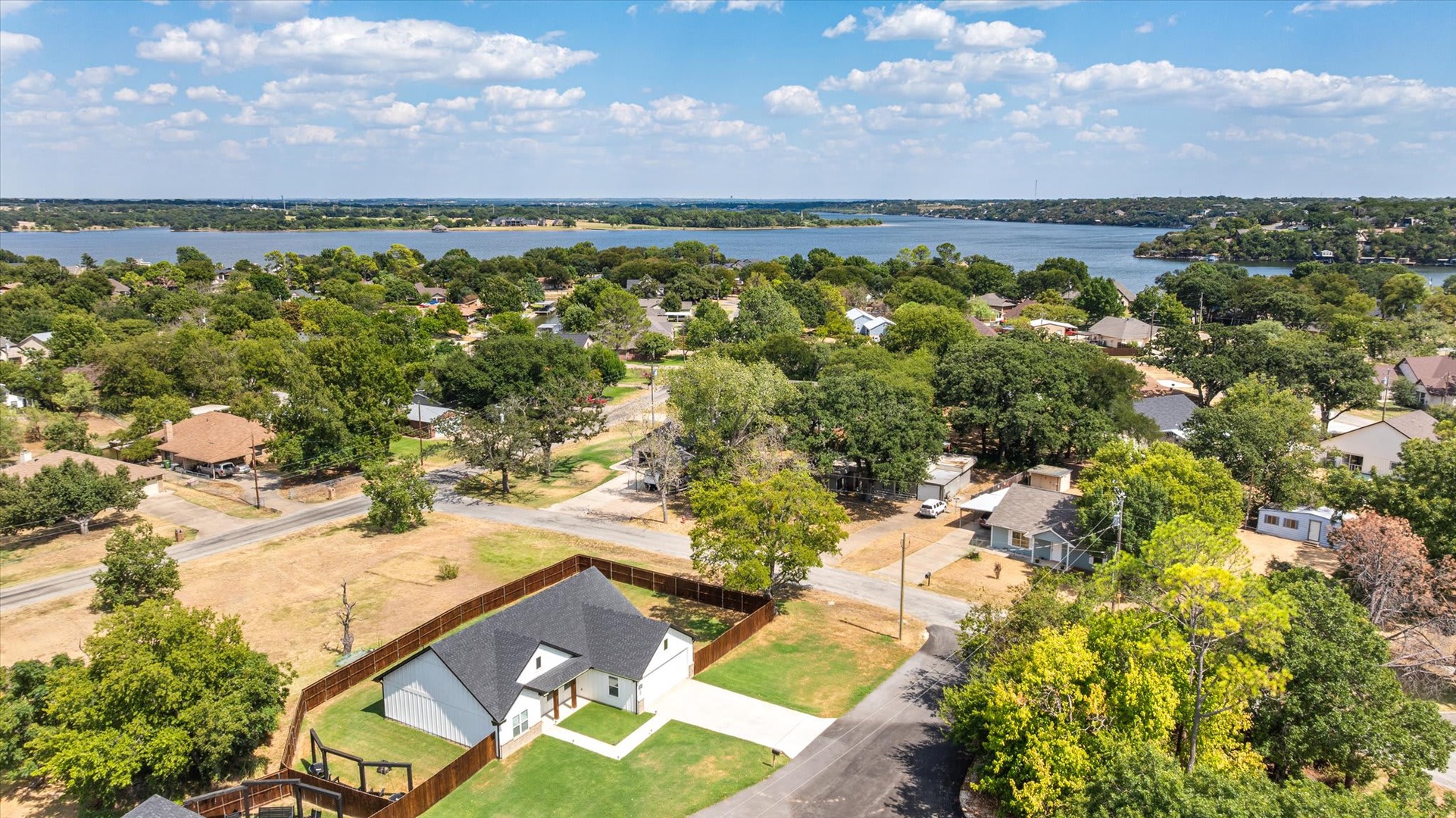 Aerial view of the property situated in a peaceful lakeside neighborhood, with mature trees and water views visible beyond the residential area.