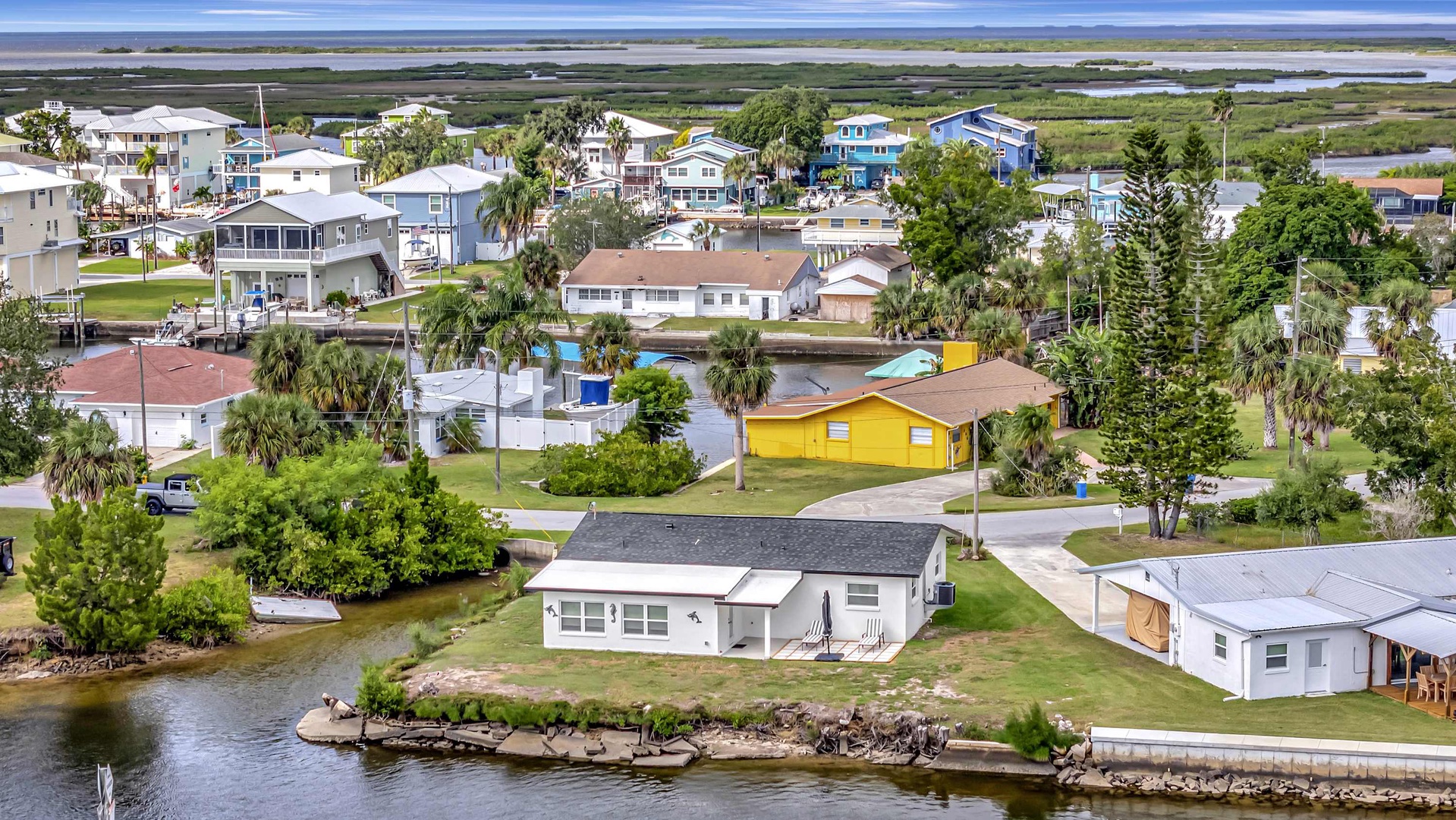 Aerial view of a waterfront coastal community with diverse vacation homes, lush palm trees, and direct access to marshlands and the bay beyond.
