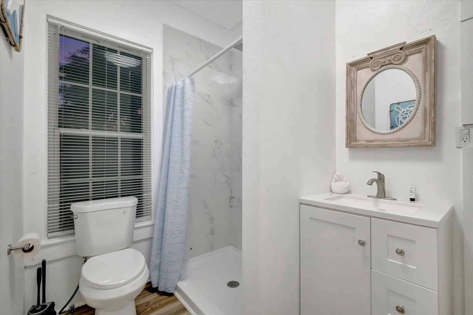 Step into your pristine bathroom with bright marble-style finishes, refreshing shower, and nautical-inspired décor that brings a hint of coastal charm to your morning routine.