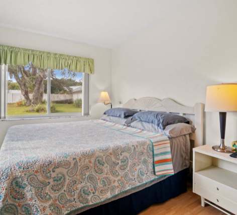 Wake up in this peaceful bedroom with natural light streaming through the window, overlooking a grassy lawn and coastal trees—your serene retreat by the sea.