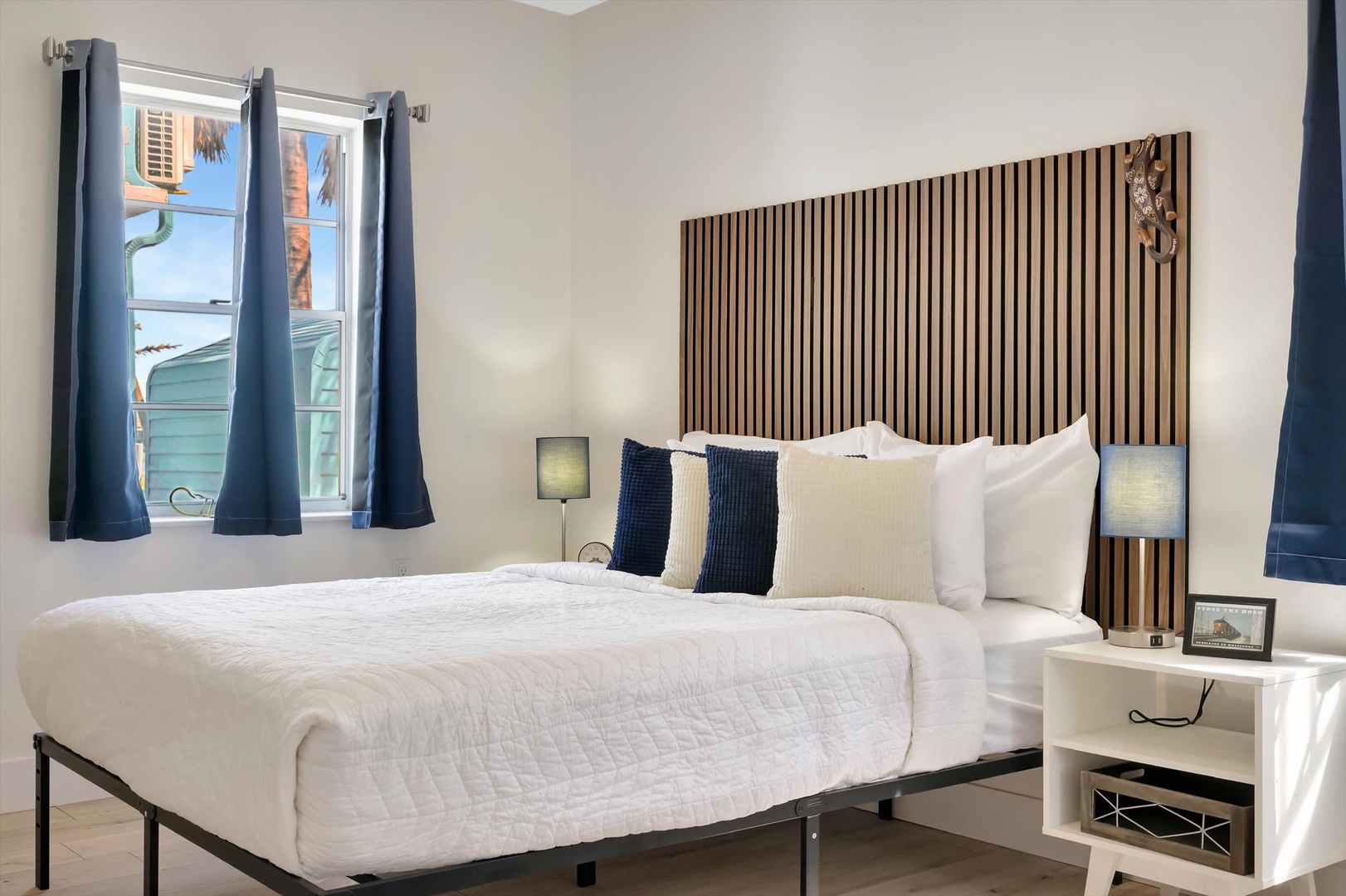 Drift off in your serene bedroom, where crisp white linens meet a striking wooden headboard. Natural light filters through soft curtains as you settle in for a peaceful night's rest.