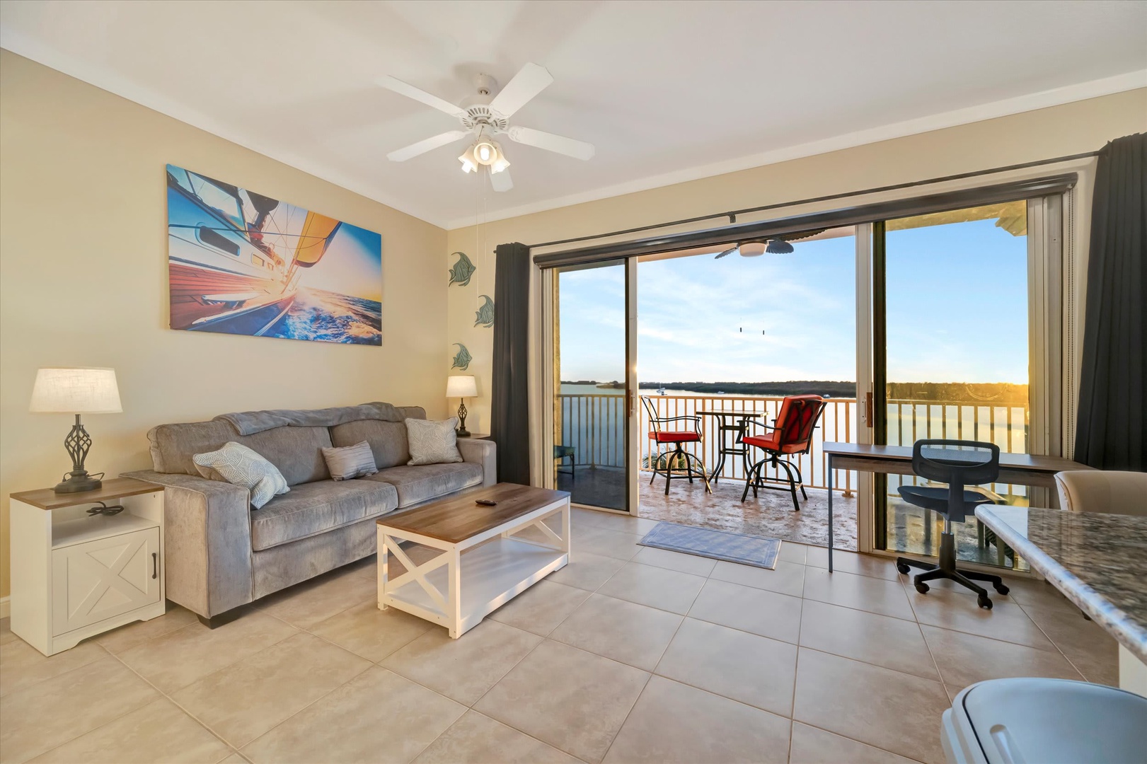 Relax in your inviting living space with a ceiling fan overhead, opening to a private waterfront balcony where you can watch the water shimmer under bright blue skies.