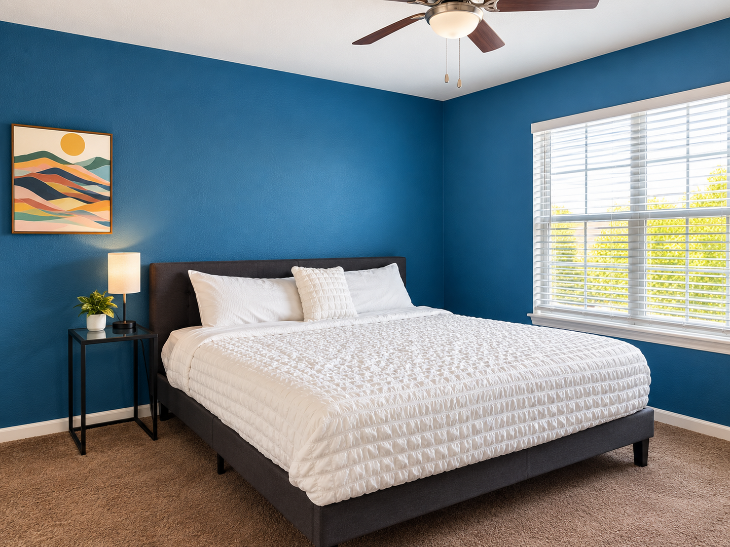 Sink into your plush bed surrounded by soothing blue walls and natural light streaming through the window. Your ceiling fan keeps the air fresh while colorful artwork adds a cheerful touch to your restful retreat.