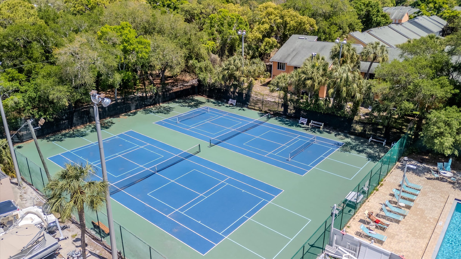 Aerial view of the tennis courts and pool area surrounded by lush tropical landscaping, perfect for active getaways.