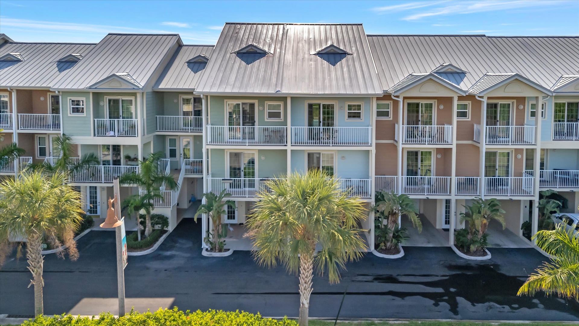 Multi-unit beach property with metal roofs and palm trees, featuring ground-level parking and private balconies for each unit.
