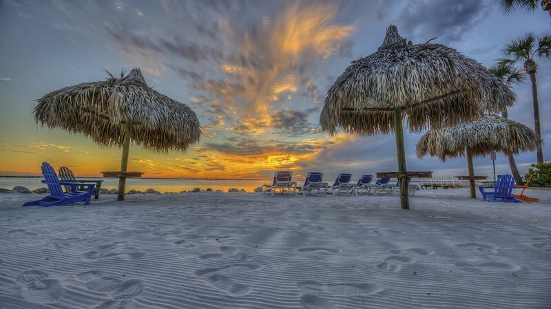 A stunning sunset paints the sky over the private beach, where thatched palapas and lounge chairs await your perfect evening by the water.