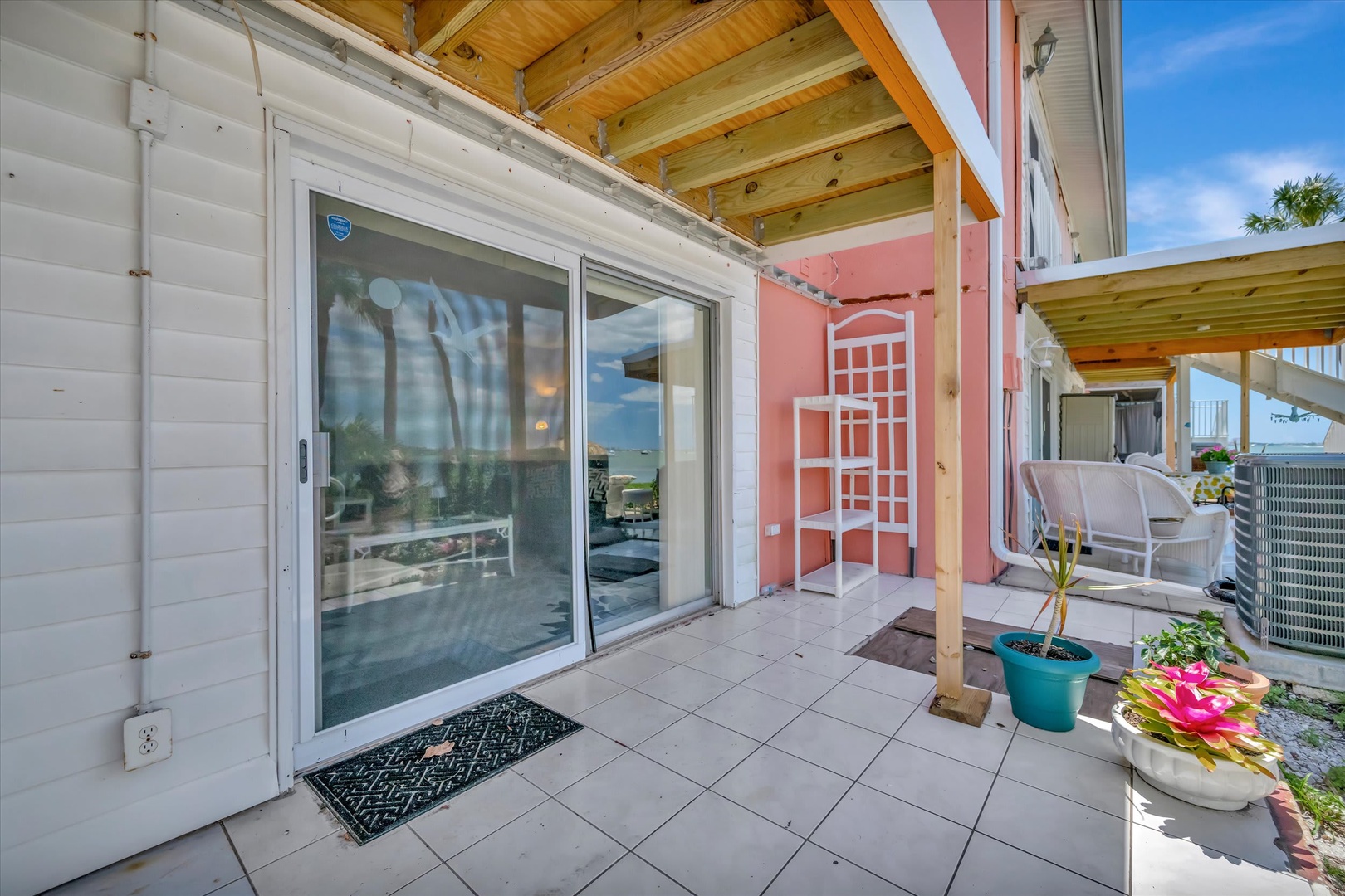 This charming covered patio welcomes you with coastal style and relaxed island vibes. Enjoy your morning coffee in the fresh air, surrounded by vibrant potted plants and easy access to your private retreat.