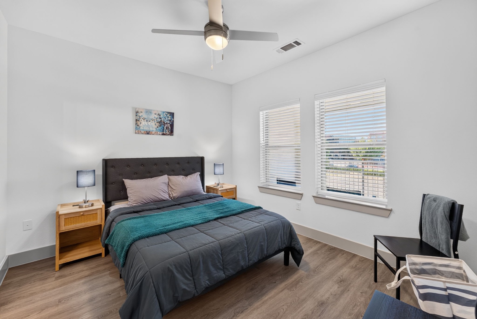 Drift off in your bright, modern bedroom with plush bedding, warm wood floors, and a gentle ceiling fan overhead—your peaceful escape awaits.