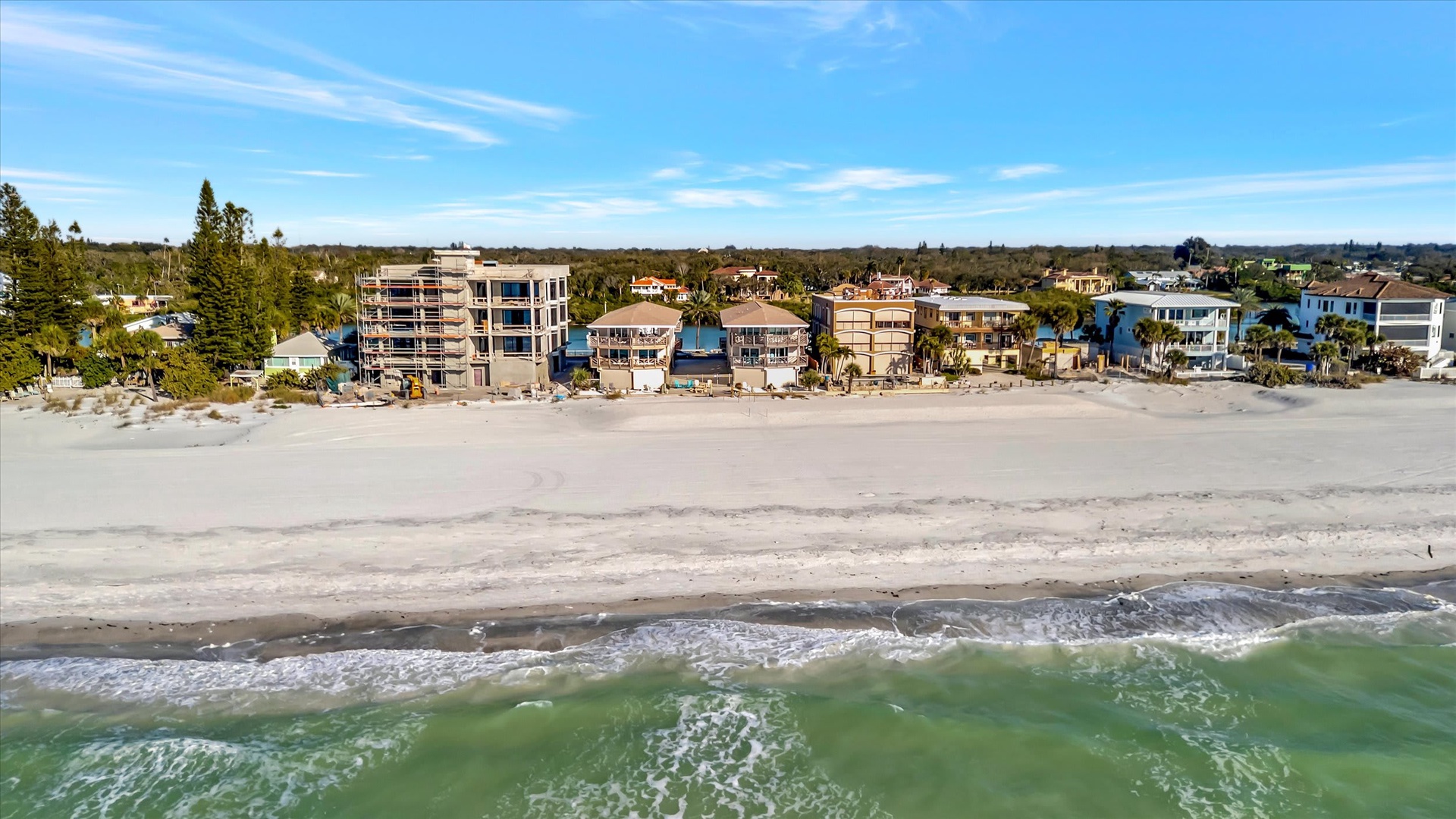 Aerial view showcasing the beachfront location, with soft sand and gentle surf just steps from the property entrance.