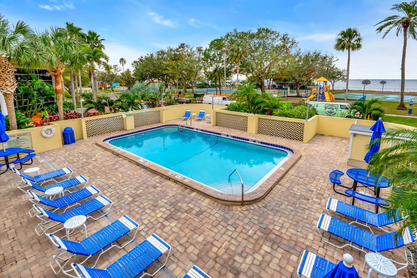 The sparkling pool awaits, surrounded by lounge chairs and tropical palms. Beyond, a playground and waterfront views promise sunny days full of fun and relaxation for you and your family.