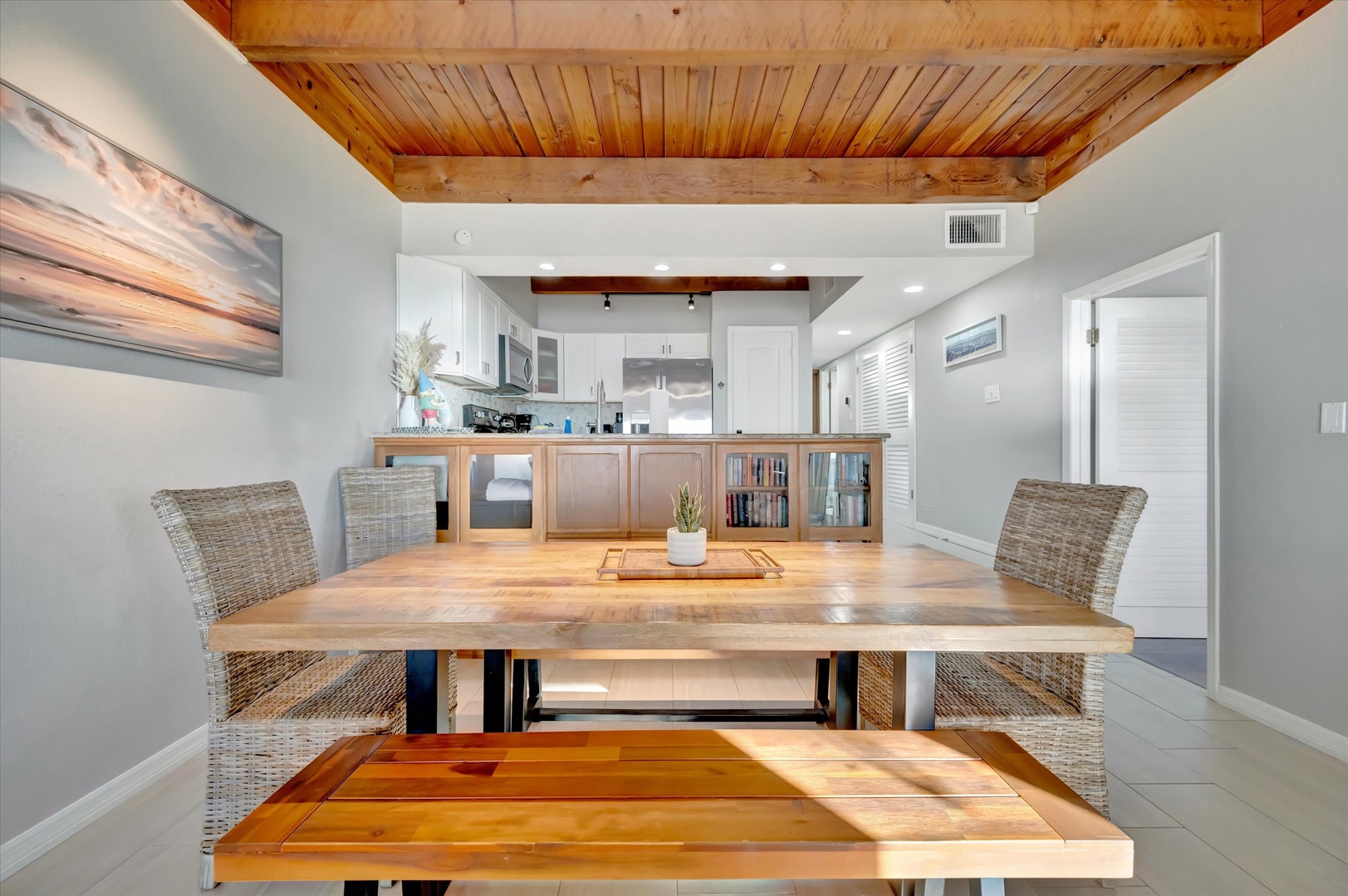 Gather around the handcrafted wood dining table under warm exposed beams, where natural light and coastal charm set the scene for your memorable meals together.
