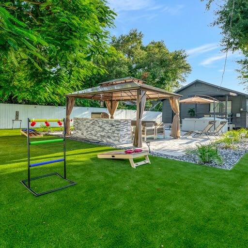A spacious backyard features lush green lawn, a shaded gazebo with outdoor seating, and lawn games ready for your enjoyment under sunny skies.