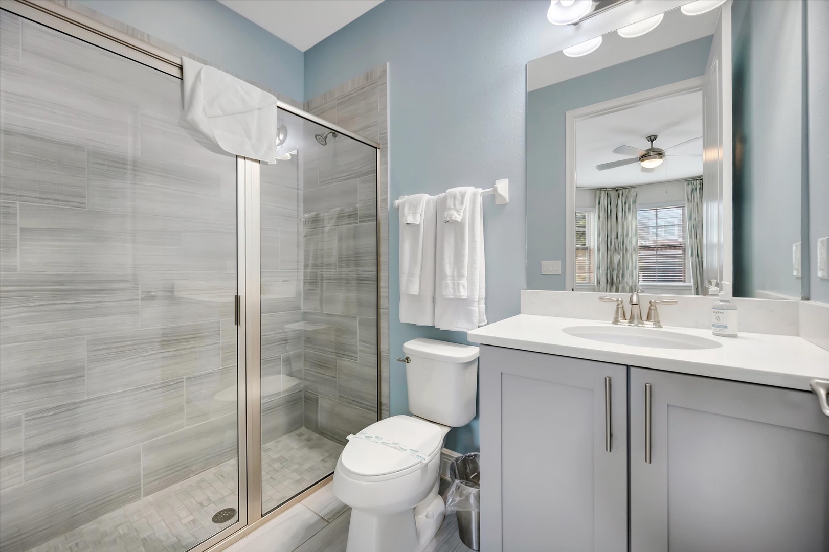 Freshen up in your private spa-like bathroom, featuring a sleek walk-in shower, crisp white linens, and calming coastal tones that invite relaxation.