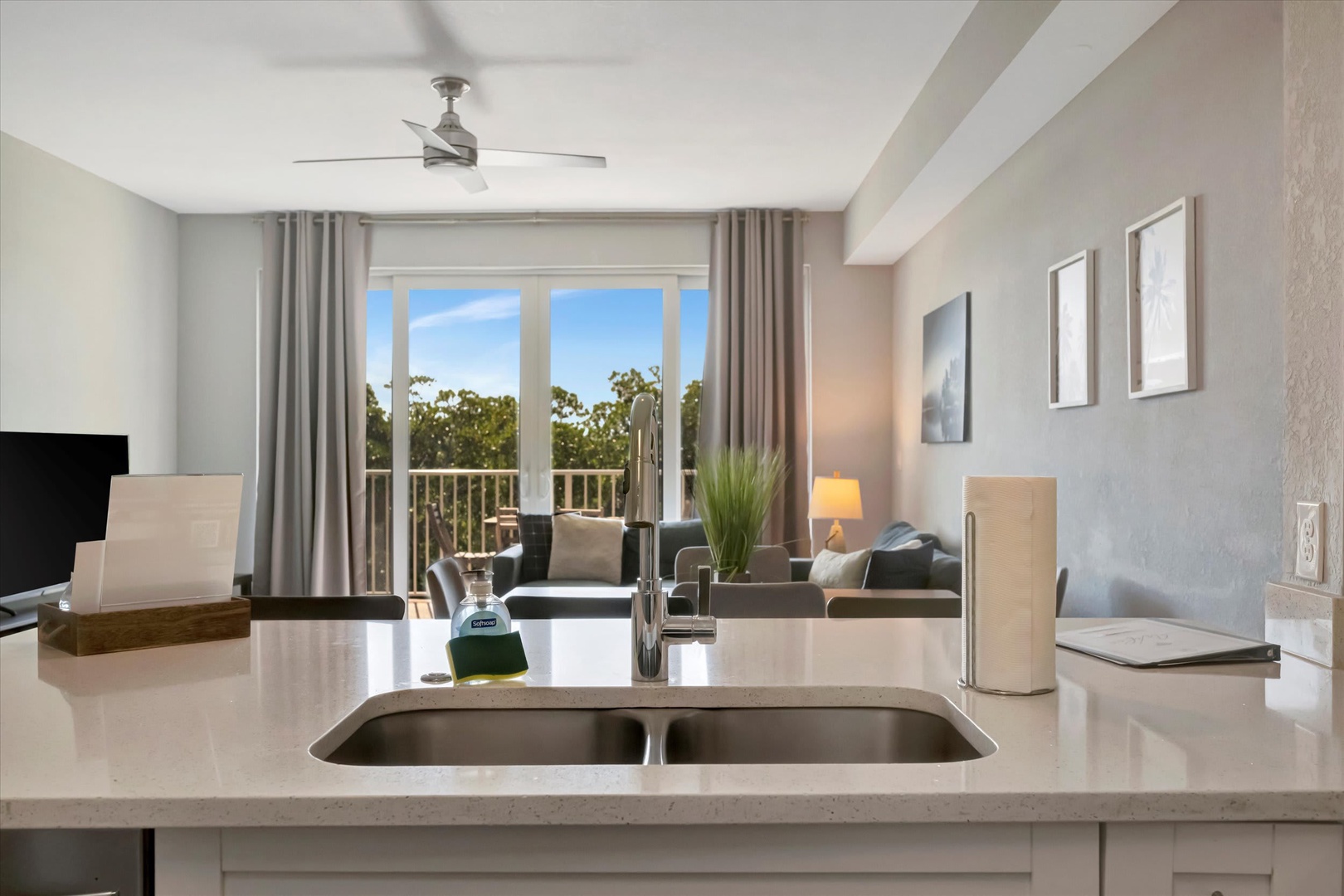 Bright, open living space with a fully equipped kitchen island flowing into a cozy sitting area. Step out to your private balcony and enjoy the lush treetop views.