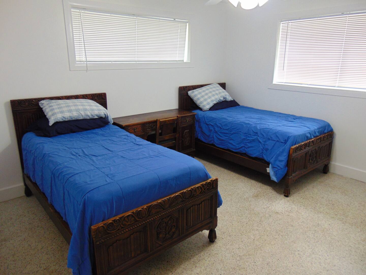Rest easy in this bright twin bedroom, where natural light filters through double windows to awaken your mornings. Rich wooden beds dressed in blue add warmth to your peaceful retreat.