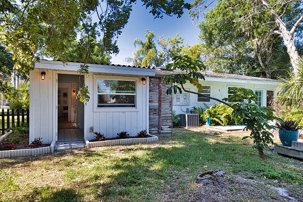 A charming cottage-style property surrounded by lush tropical greenery, offering a peaceful retreat with shaded garden spaces and an inviting front entrance.