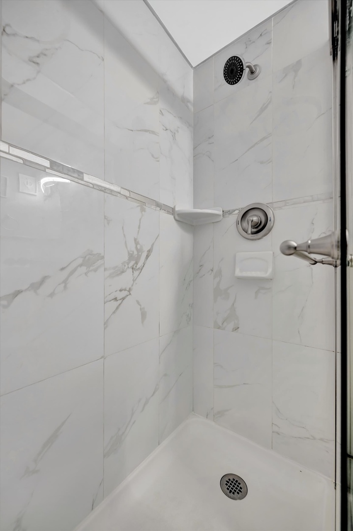 Step into your pristine marble-look shower with dual fixtures and a spacious, modern design perfect for refreshing mornings.